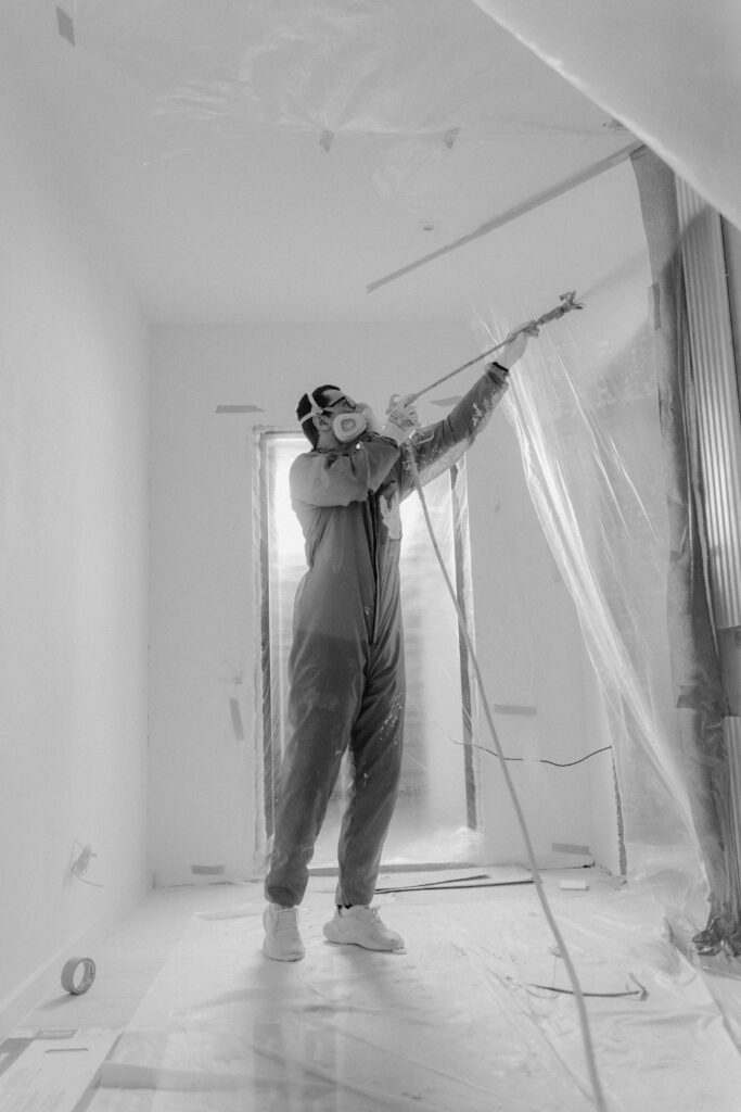 A worker in a respirator uses a spray gun on a construction site during renovation.